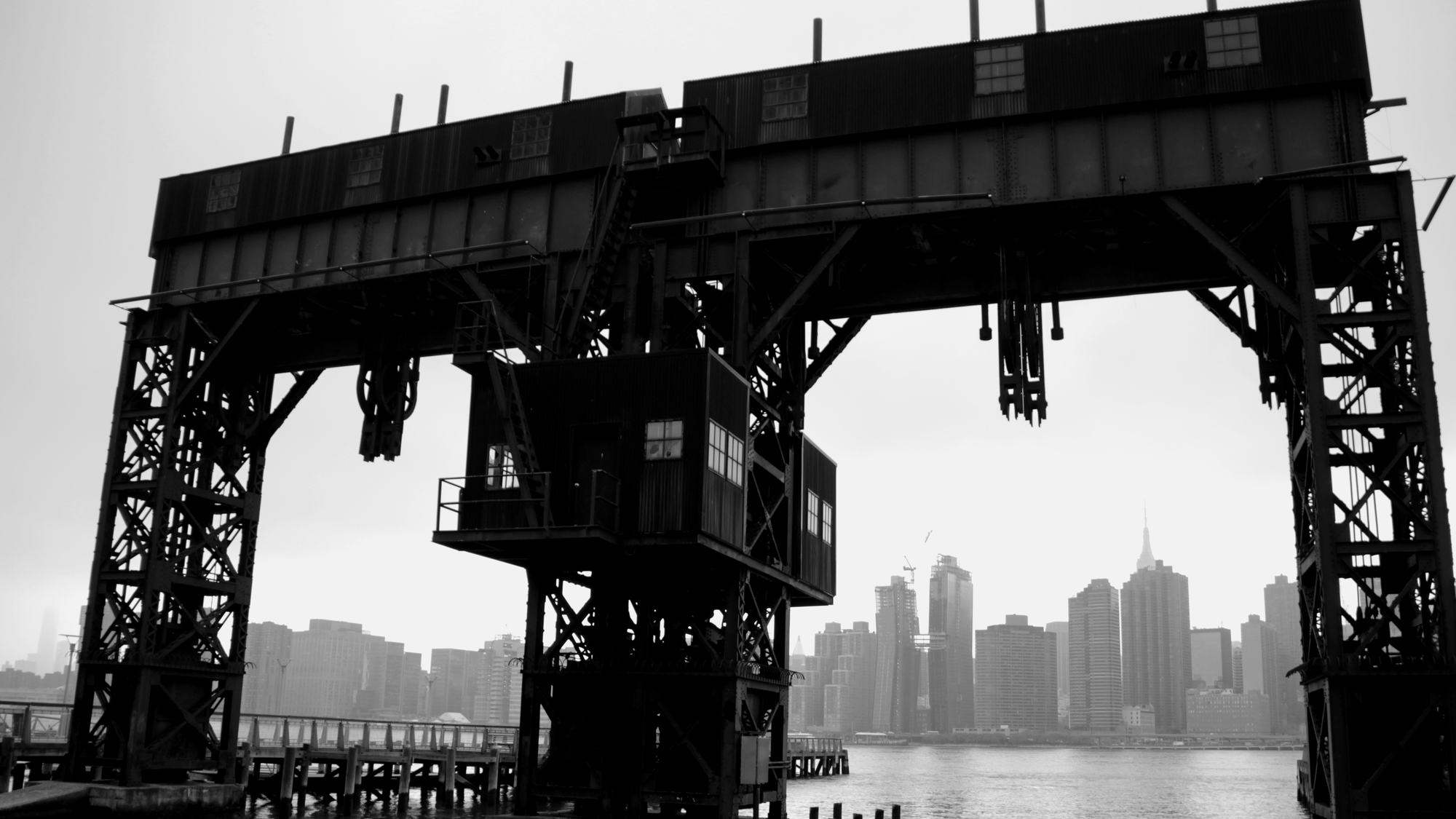 A steel gantry on the Long Island City waterfront framing the Midtown Manhattan skyline